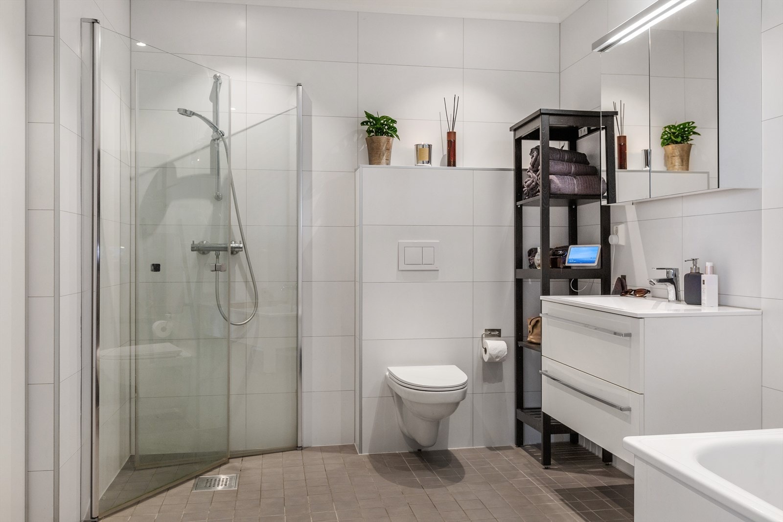 Badet er innredet med hvit baderomsinnredning med skuffer, vegghengt toalett, badekar og dusjhjørne med innfellbare dusjvegger Galleribilde