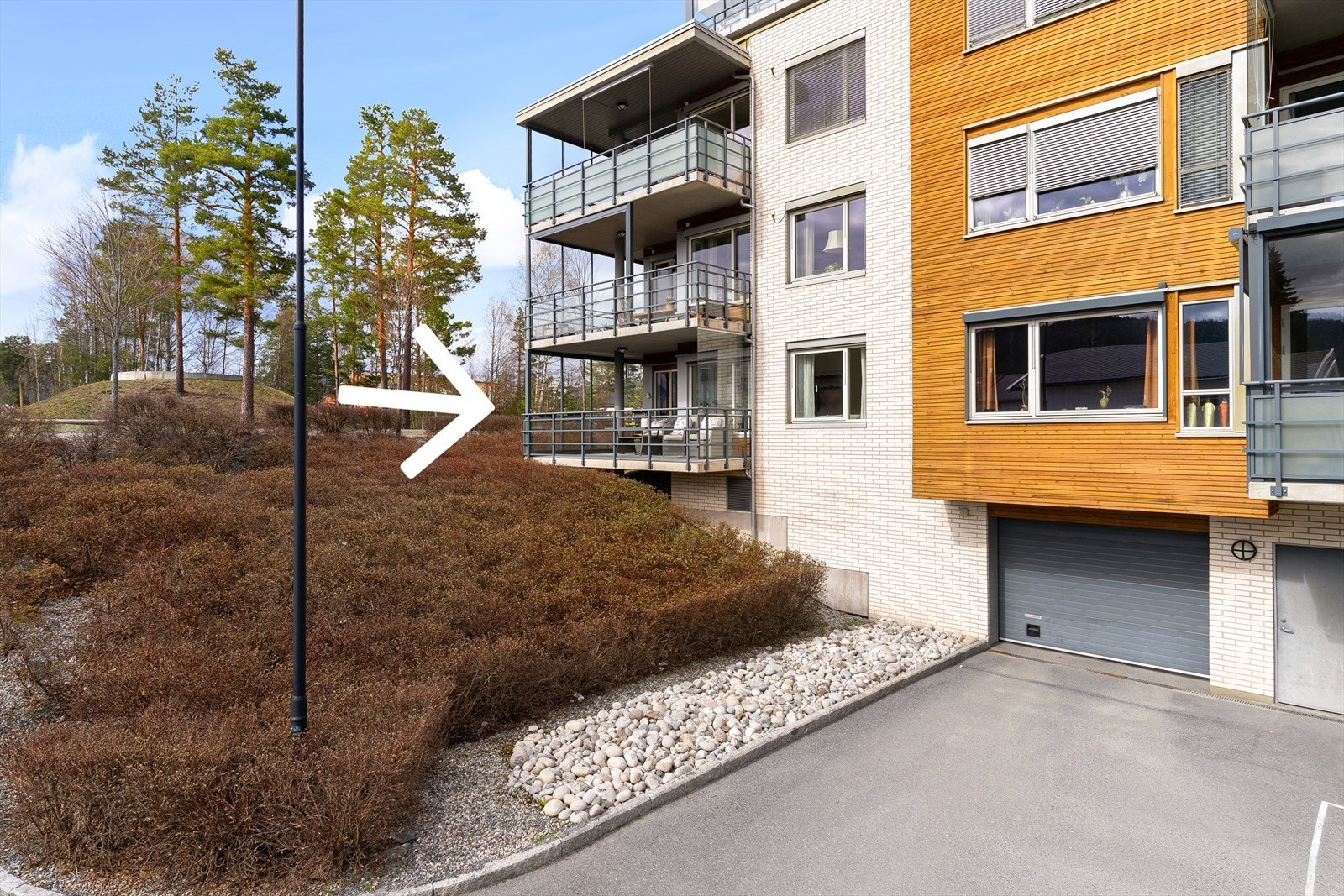 Leiligheten ligger som hjørneleilighet i byggets andre etasje. Innkjøringen til garasjeanlegget har man ned til høyre. Galleribilde