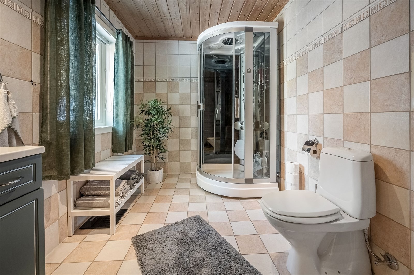 Stort og flislagt bad som består av profilert baderomsinnredning med servant og benkeplate, speil med belysning, dusjkabinett med massasjefunksjon og toalett. Galleribilde