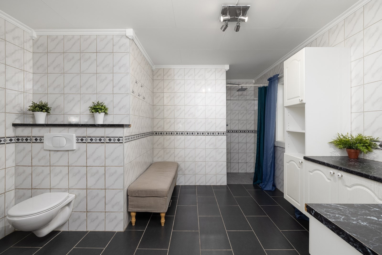 Badet er innredet med servant på innredning, vegghengt toalett og dusjnisje med forheng. Galleribilde