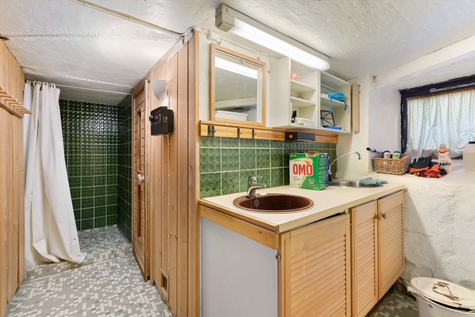 Baderommet i kjelleren har en enkel standard med mosaikkfliser på gulvet og vegger av pusset mur og panel. Galleribilde