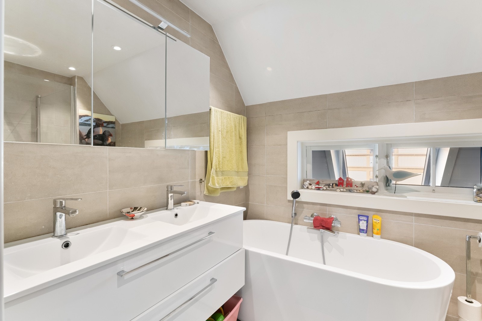 Badet var nytt rundt 2016 og er innredet med delikate, beige fliser på vegger og gulv. Det er gulvvarme, downlights, elektrisk styrt vifte og dagslys via et smalt vindu som vender ut mot takvinduet på kjøkkenet. Galleribilde