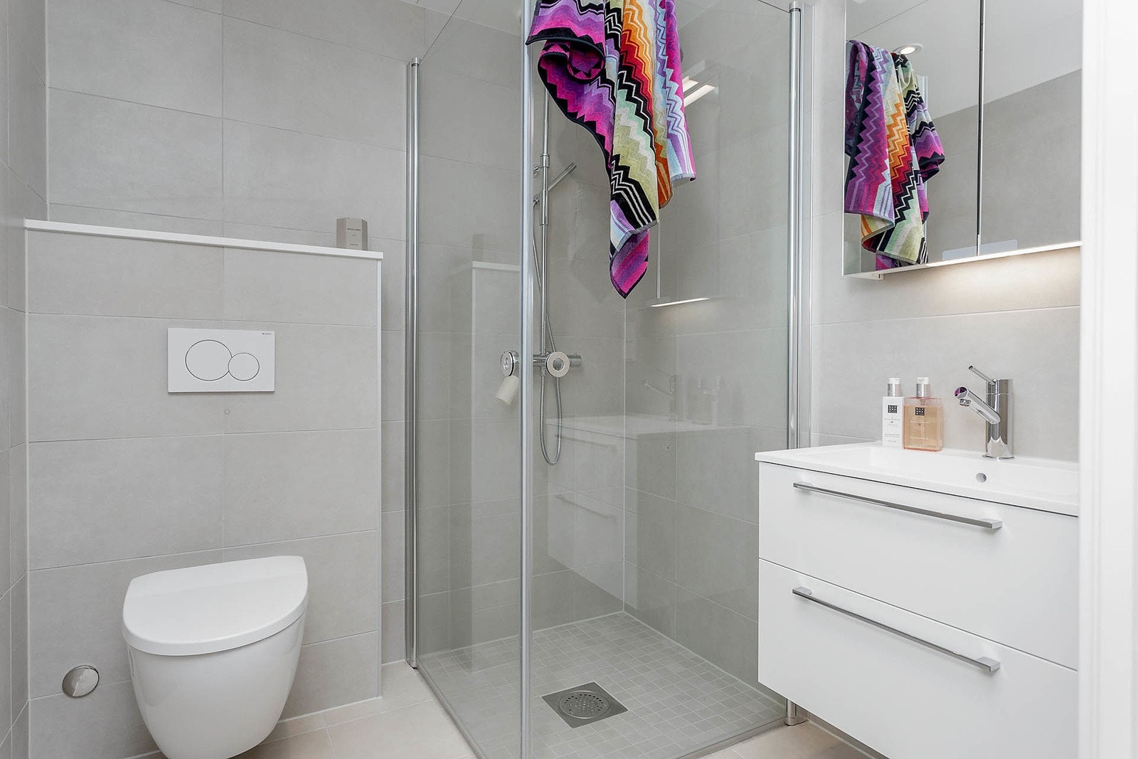 Bad i tilknytning soverom 1 er delikat og moderne. Badet inneholder servant med skuffeseksjon, veggspeil med belysning, dusjhjørne med svingbare glassdører samt vegghengt wc. Galleribilde