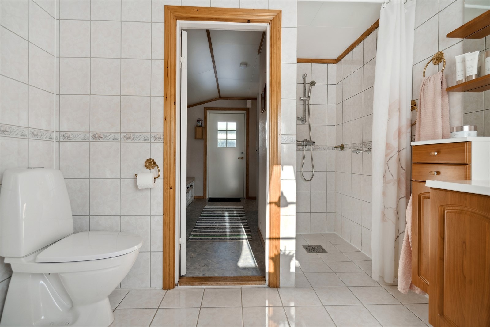 Badet er flislagt og er utstyrt med toalett, innredning, opplegg for vaskemaskin og dusjnisje Galleribilde