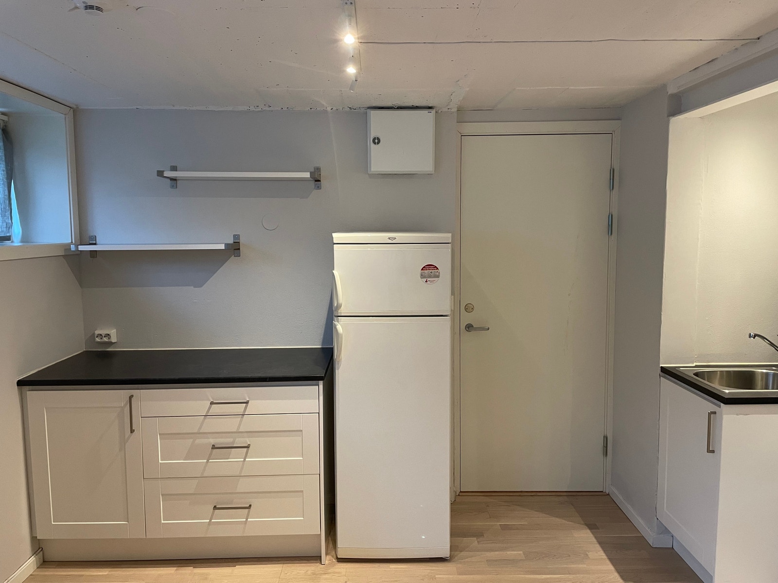 Kjøkken med stor arbeidsbenk. God plass i skuffene til kjøkkenutstyr. Ved siden av benken er det plassert et kjøleskap m/fryser. Hyller er montert over benk. Galleribilde