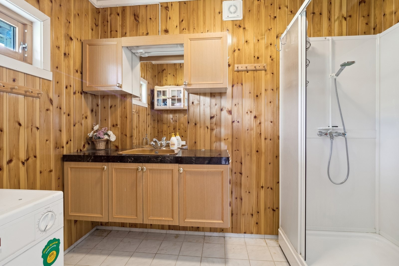 Baderomsinnredning med profilerte fronter og benkeplate med nedfelt servant, speil med belysning og vegghengte skap over. Baderommet er også utstyrt med dusjkabinett, toalett og opplegg for vaskemaskin. Galleribilde