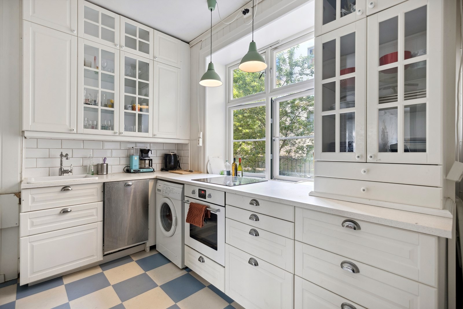 Lakkerte 1-speils profilerte formpressede fronter, 8 stk. glassfronter i overskap, laminat benkeplate m/fliser over en benk, enkel keramisk oppvaskkum, integrert koketopp, stekeovn og oppvaskmaskin, samt frittstående kjøl-/fryseskap Galleribilde