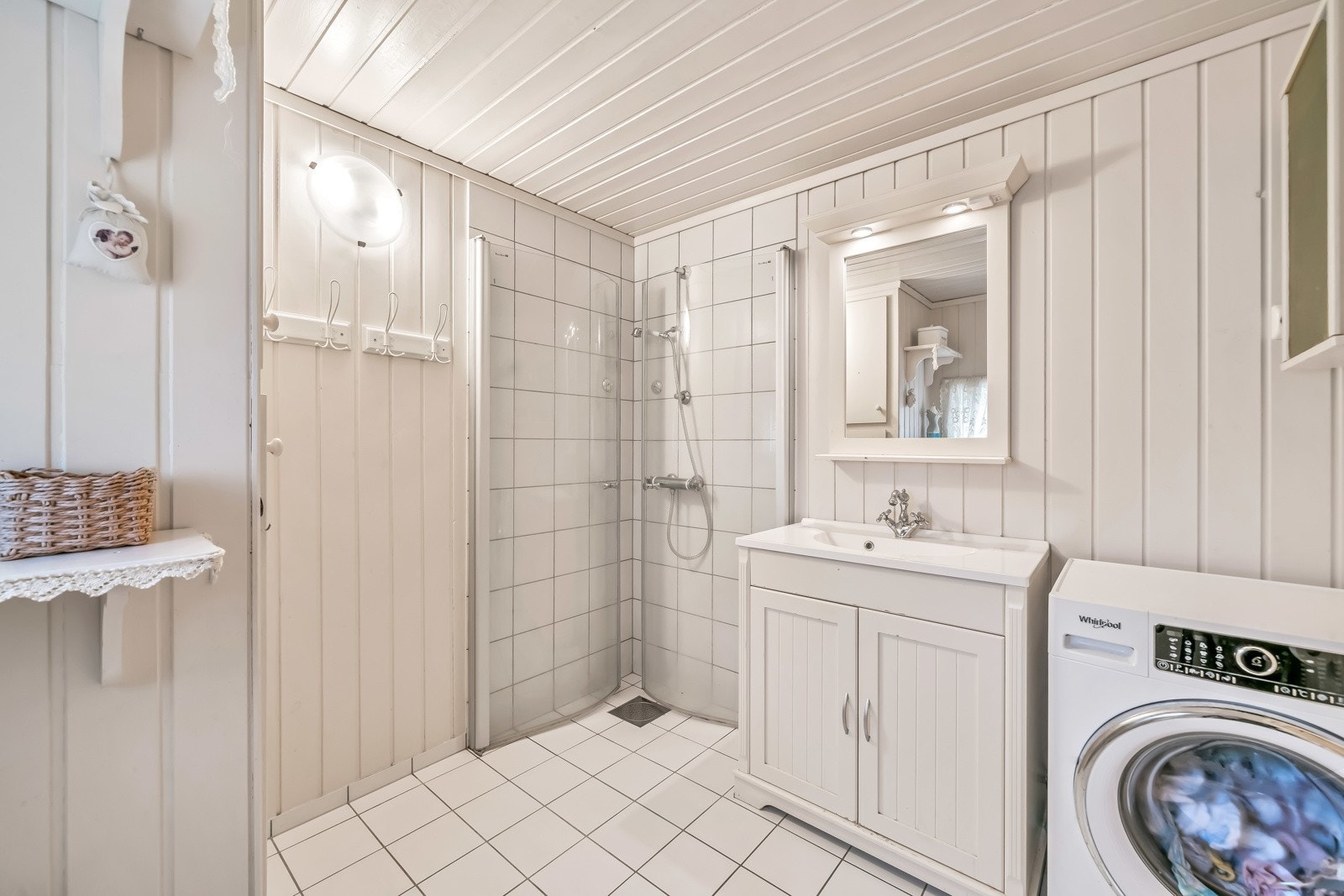 Pent bad innredet med fliser med varmekabler på gulv og panel/fliser på vegg. Badet er innredet med baderomsinnredning, toalett, dusjløsning og opplegg til vaskemaskin. Galleribilde