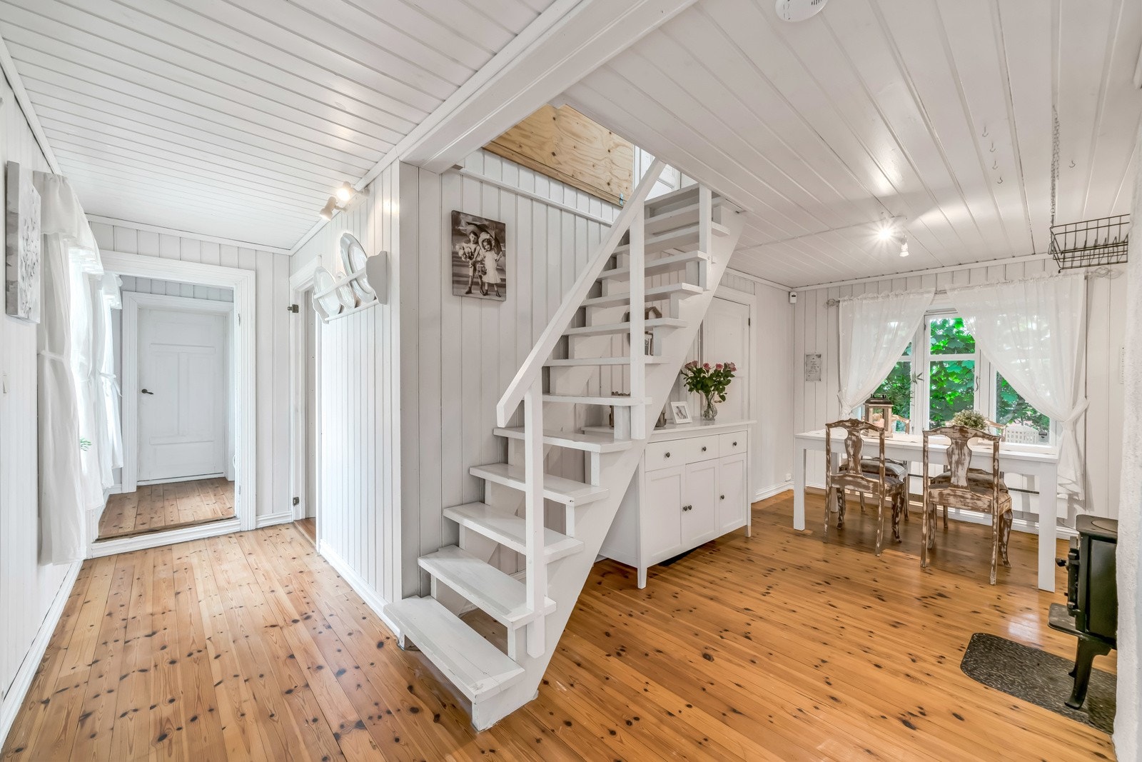 Mellom stua og kjøkkenet er det en mellomgang med flere bruksmuligheter. Her kan man etablere en kosekrok ved vedovnen på motsatt side, eller anrette med spisebord slik det er i dag. Galleribilde
