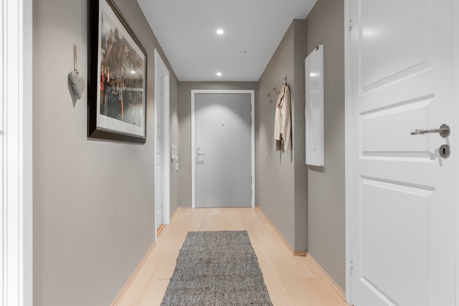 Veggene i èntreen er malt i en smakfull gråfarge som harmonerer godt med øvrige rom, og rommet har også enstavs parkett på gulv med varme og downlights i hvit himling. Galleribilde