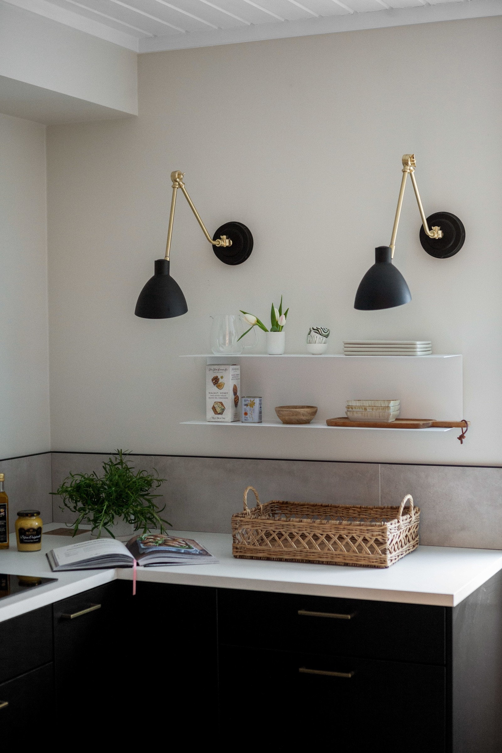 Kjøkkeninnredningen fra Huseby har sorte, glatte fronter, vitrineskap, hvit benkeplate av laminat med integrerte messing stikk, svart oppvaskkum og messing armatur. Galleribilde
