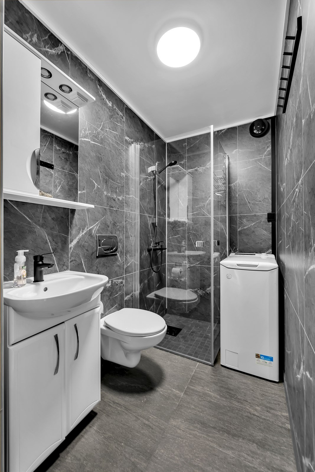 Badrom med 60x60 gulvfliser, vegghengt toalett og dusjnisje med glassdører.