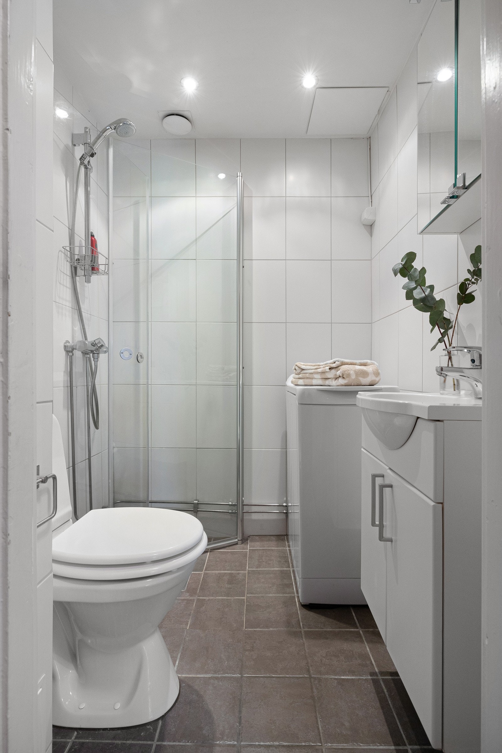 Flislagt baderom med gulvvarme, dusjhjørne, klosett, servant og opplegg for vaskemaskin. Galleribilde