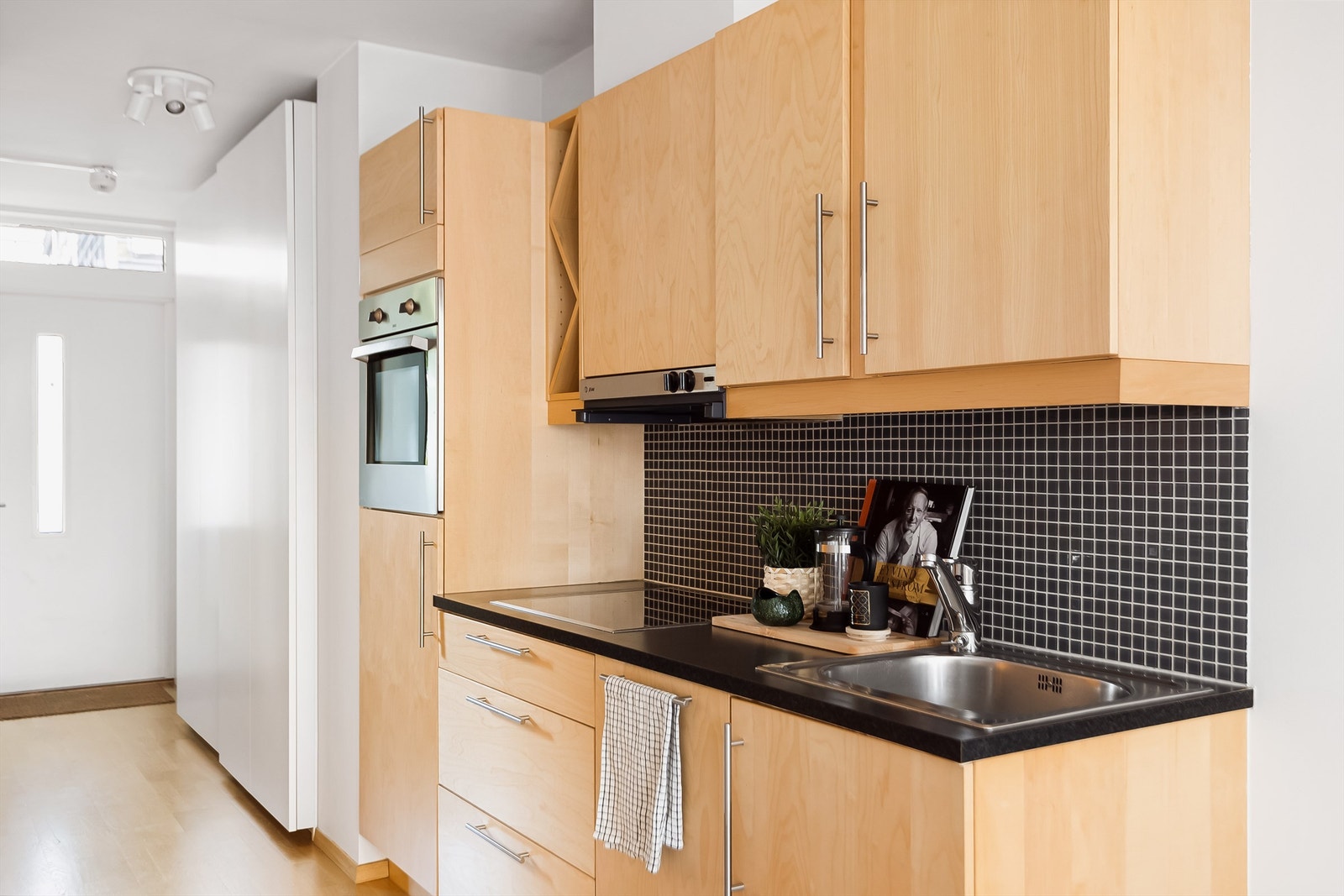 Effektivt kjøkken med integrerte hvitevarer, fliser over benk, glatte fronter og benkeplate av laminat. Galleribilde