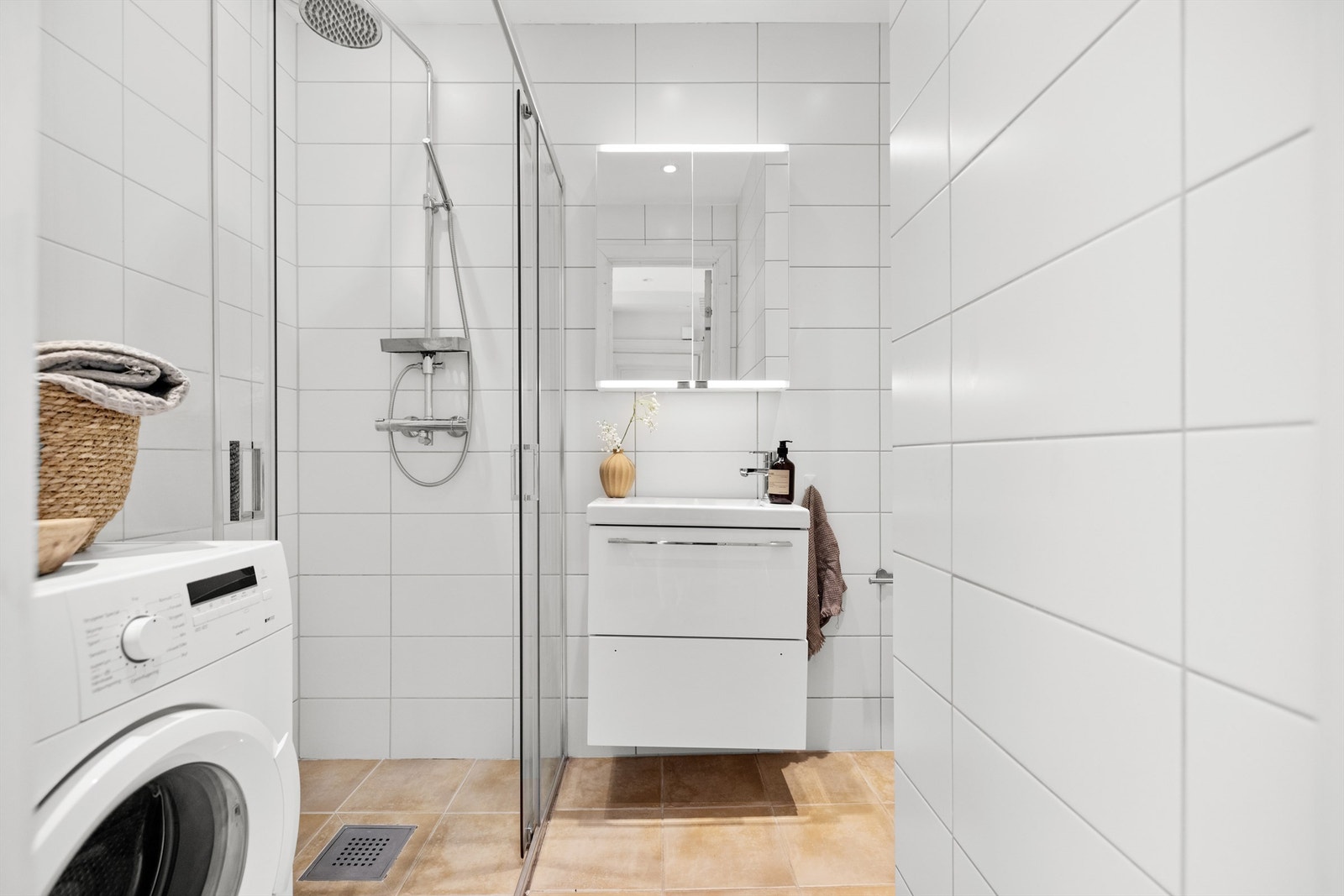 Delikat baderom fra 2015 med opplegg for vaskemaskin, flislagte gulv med gulvvarme, flislagte vegger og himlingsflater i glatte malte flater med downlights. Galleribilde