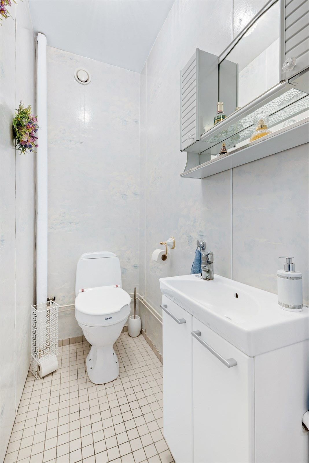 Wc med fliser på gulv, våtromstapet på vegger og malt tak. Innredningen består av wc, servant med underskap og overskap med speil. Galleribilde