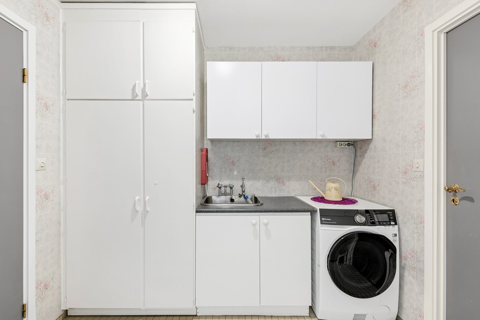 Vaskerom med fliser på gulv, våtromstapet på vegger og malt tak. Innredningen består av skapinnredning, laminat benkeplate, utslagsvask, opplegg for vaskemaskin og originalt tørkeskap. Galleribilde