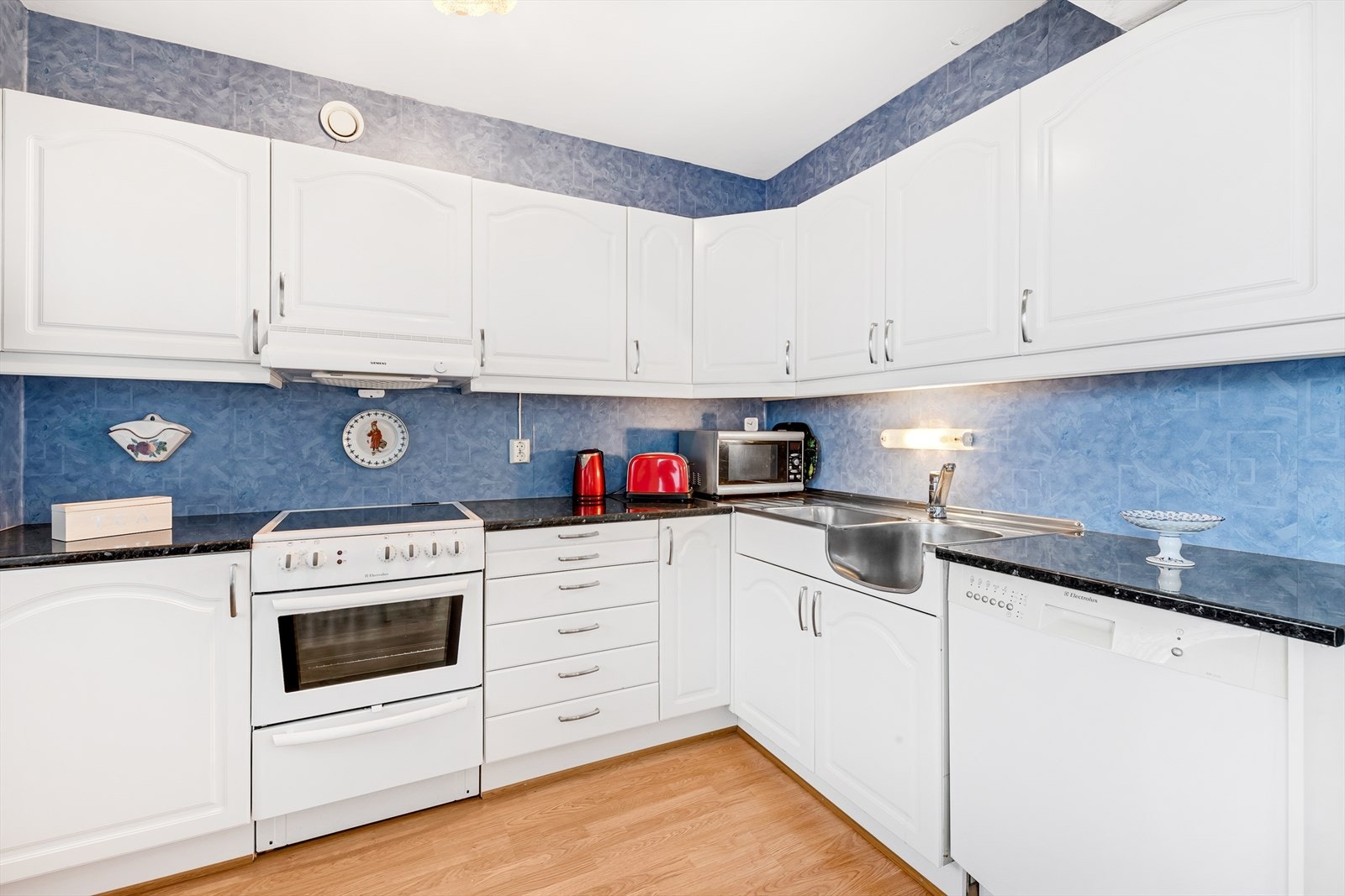 Kjøkkeninnredning med profilerte fabrikklakkerte fronter, laminat benkeplate, dobbel oppvaskkum med helt benkebeslag, ventilator, opplegg for oppvaskmaskin og varmtvannsbereder i benkeskap. Galleribilde