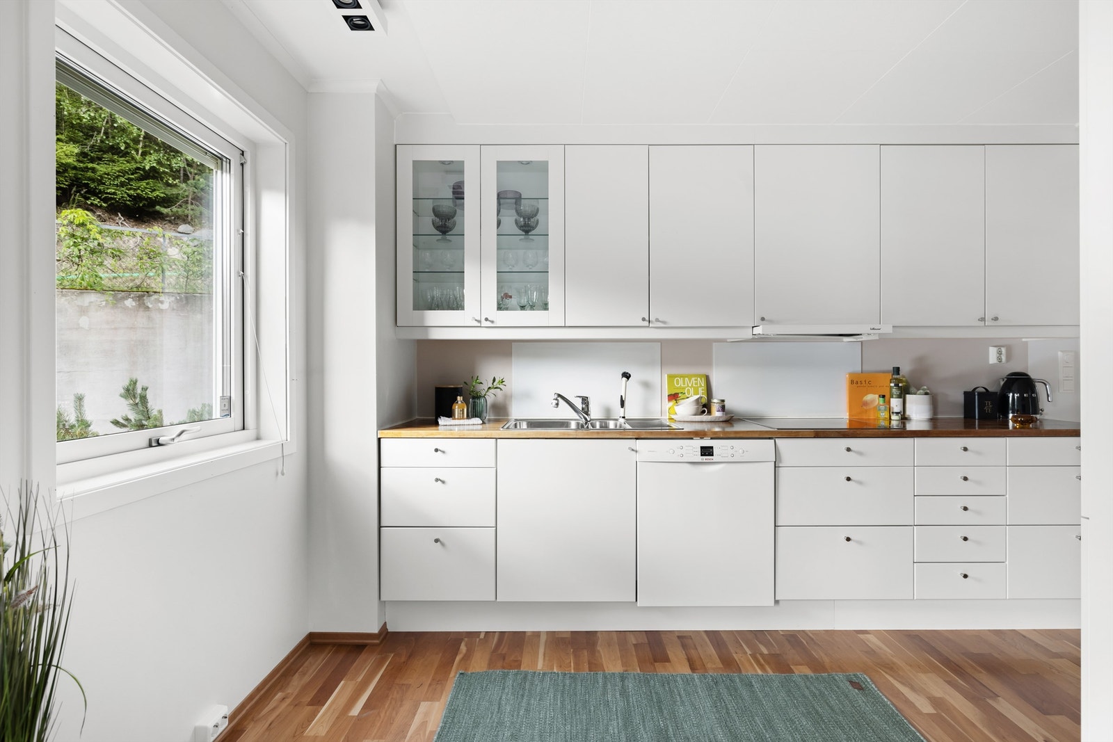 Kjøkkenet er innredet med hvite glatte fronter og laminat benkeplate med nedfelt oppvaskkum i rustfritt stål. Galleribilde