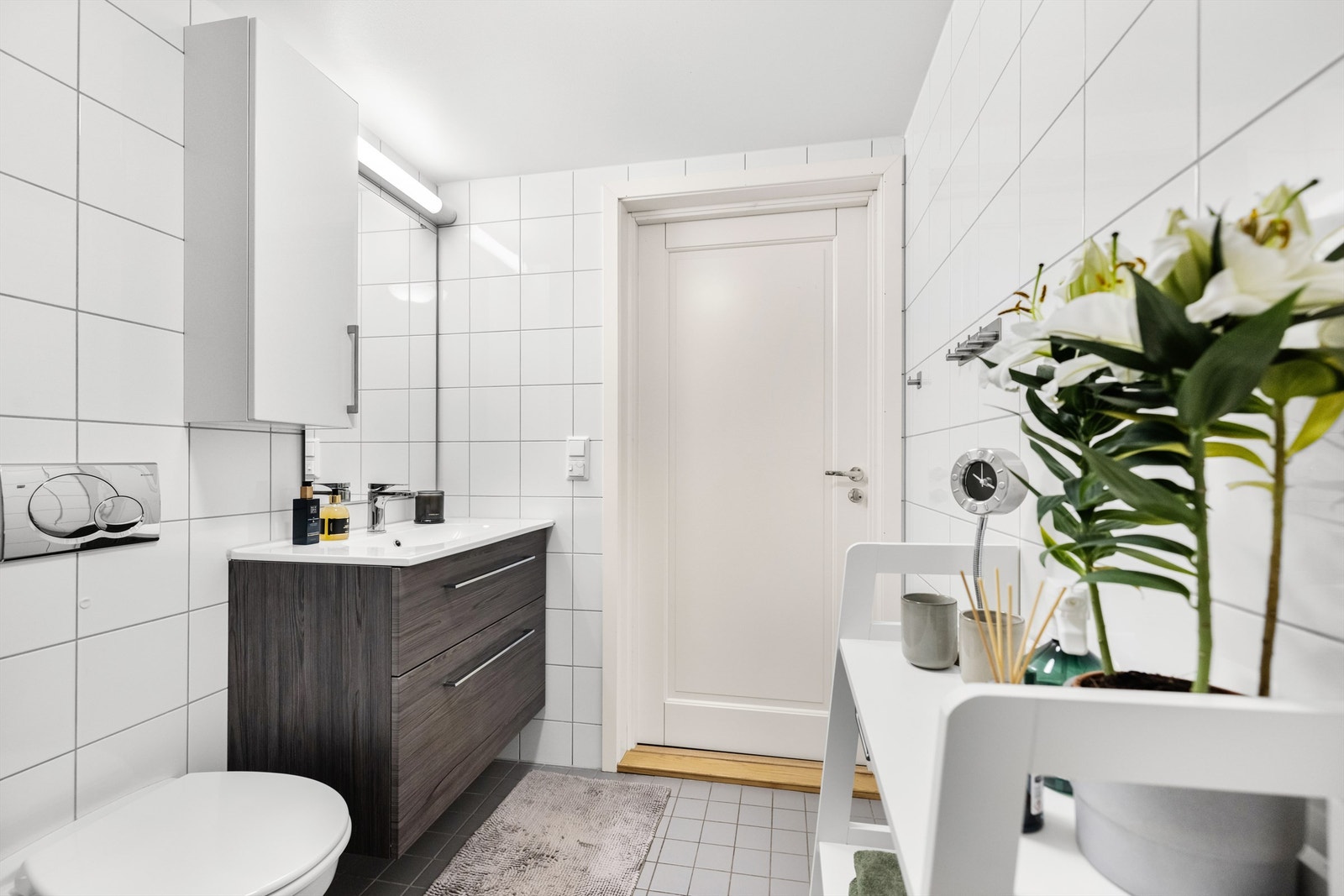 Badet er innredet med dusjvegger av glass, veggmontert toalett samt servant med tilhørende skap og speil. Galleribilde