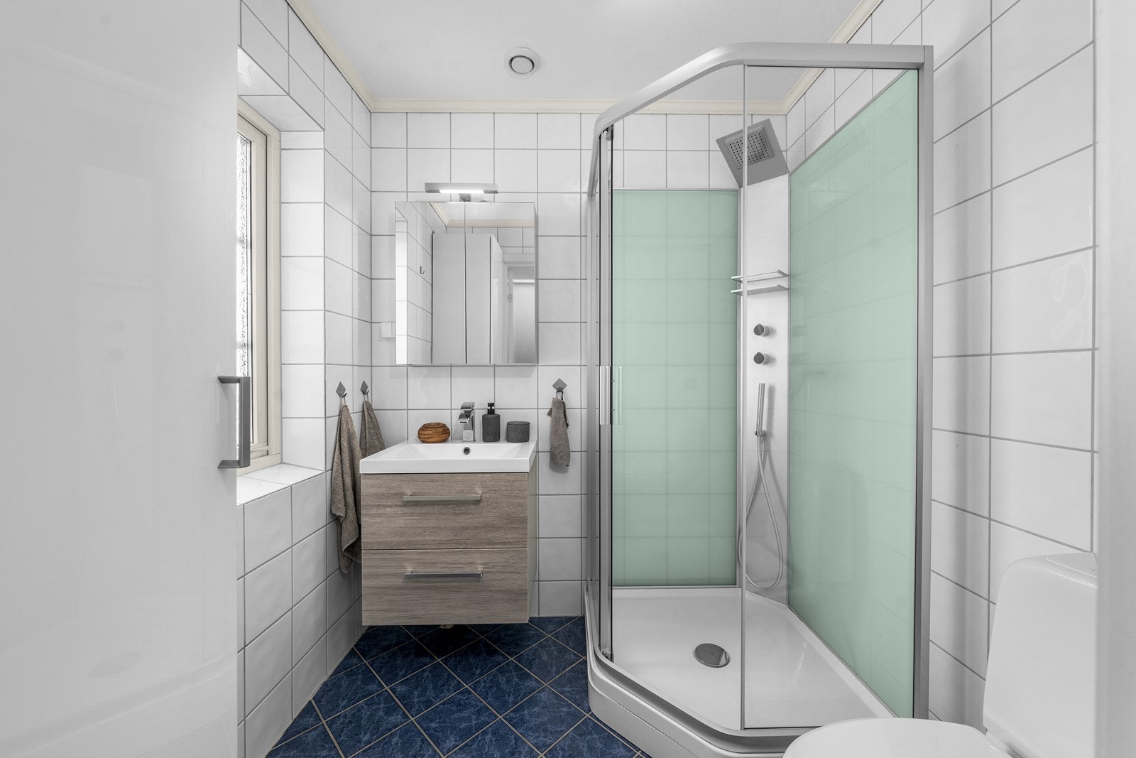 Badet i førsteetasje er flislagt med gulvmontert toalett, dusjkabinett, servantskap og speilskap med lys på vegg. Galleribilde