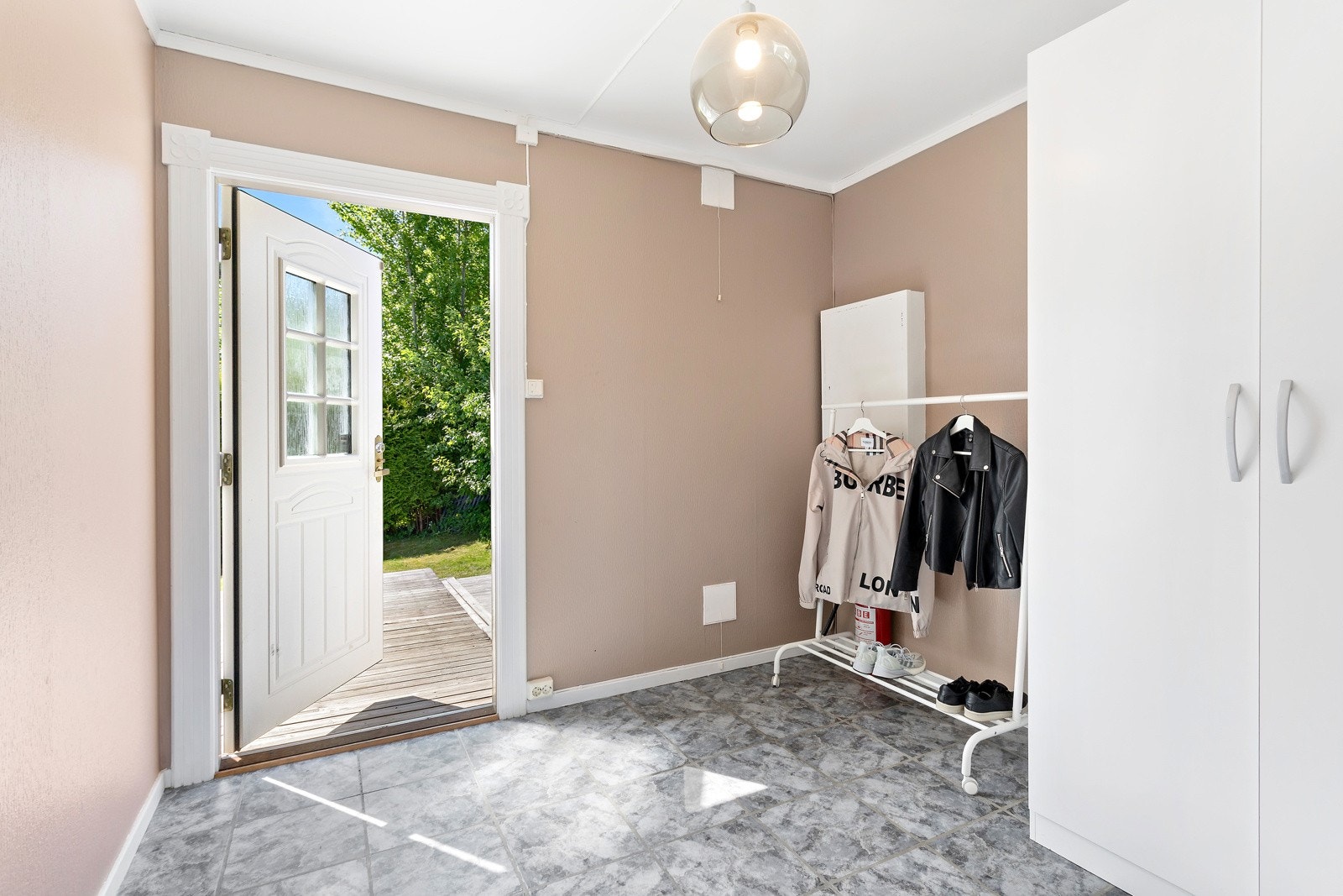 Fra terrassen på forsiden av huset kommer du inn til vindfanget hvor det er god plass til å henge fra seg yttertøy. Her har du flislagt gulv og malte slette vegger. Galleribilde