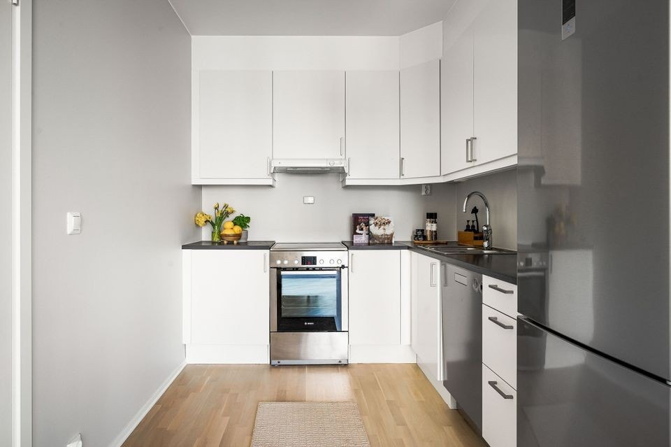 Innredning med hvite glatte skapfronter, laminat benkeplater, nedfelt rustfri oppvaskkum og ett-greps armatur. Galleribilde