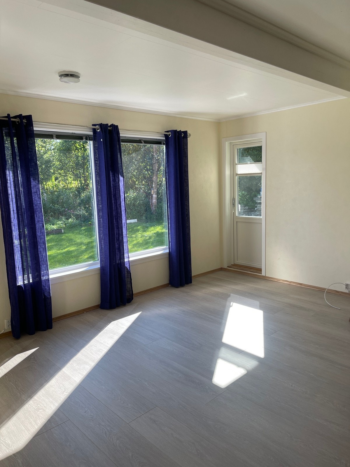 Stua med nyinnsatt balkong dør ut til platting og plen. Galleribilde