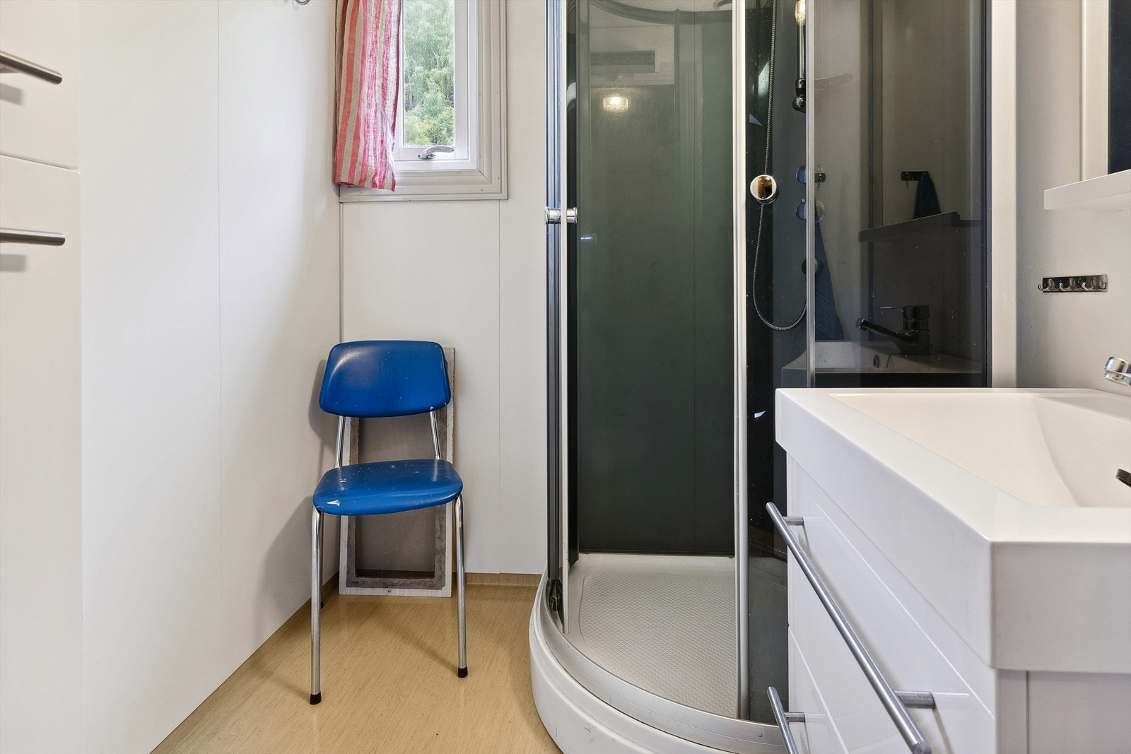 Badet består av gulvbelegg, baderomsplater på vegger og malte plater i himling. Det er montert dusjkabinett, servant med skuffer under samt høyskap på veggen. Galleribilde