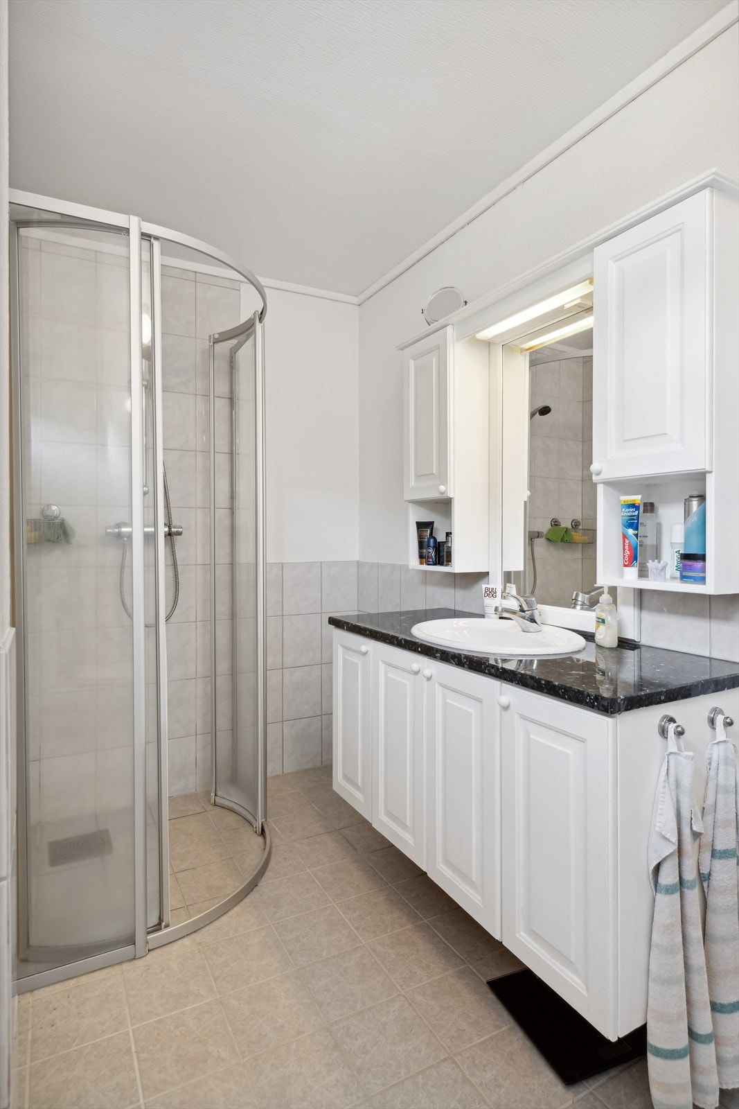 Rommet er utstyrt med gulvstående toalett, dusjhjørne og baderomsinnredning - Innredningen består av servant, underskap, overskap og speil Galleribilde