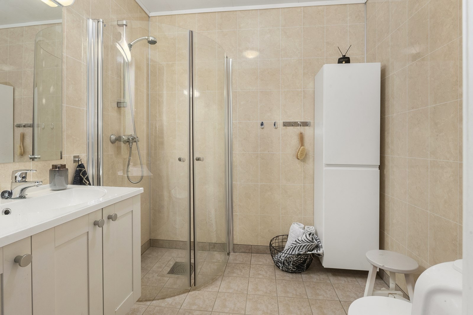 Badet har fliser på gulv med varmekabler, dusjhjørne, benkeskap og toalett. Galleribilde