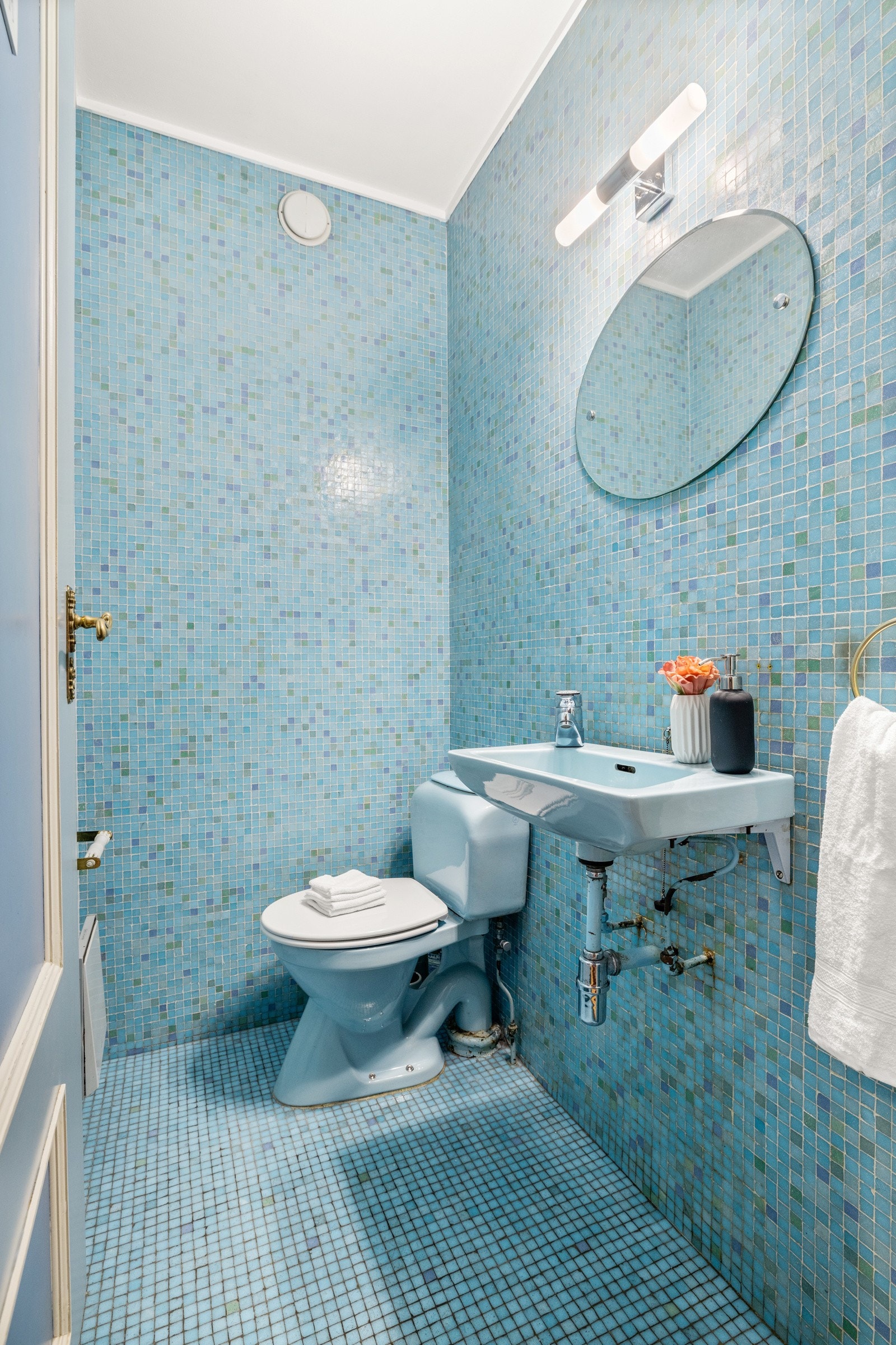 Separat WC-rom med mosaikkfliser på gulv og vegger. Gulvstående toalett og enkel servant med speil over Galleribilde