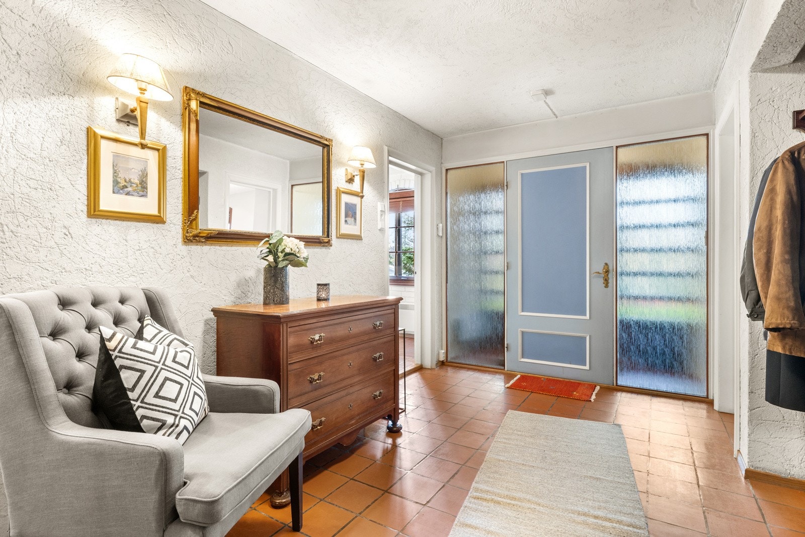 Romslig hall med flislagt gulv og glassfelter på hver side av dør til vindfang Galleribilde