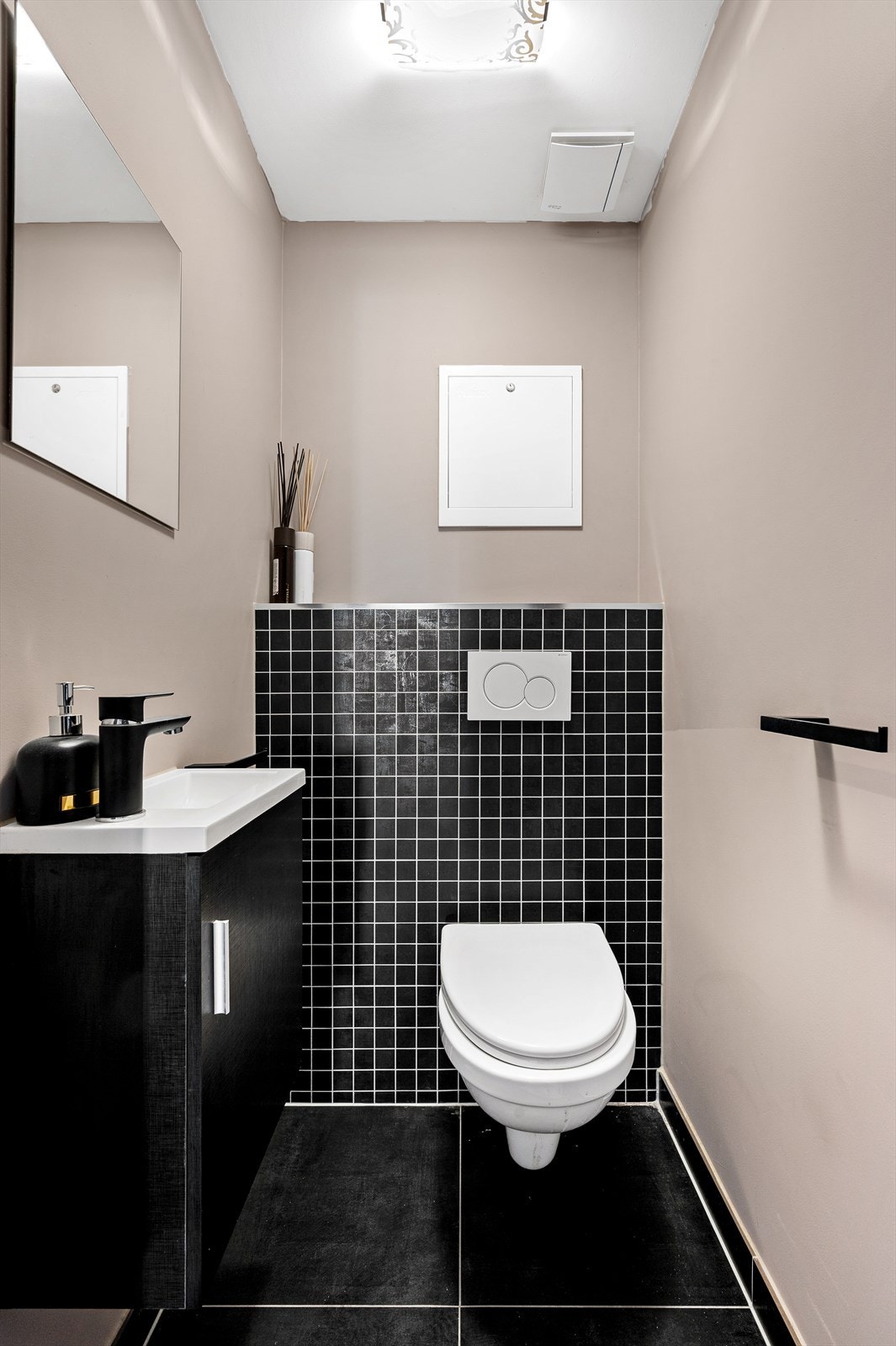 Toalettrom med flislagt gulv, varmekabler, mosaikkfliser og malte flater på vegger, belysning, avtrekk, servant med innredning og vegghengt toalett. Galleribilde