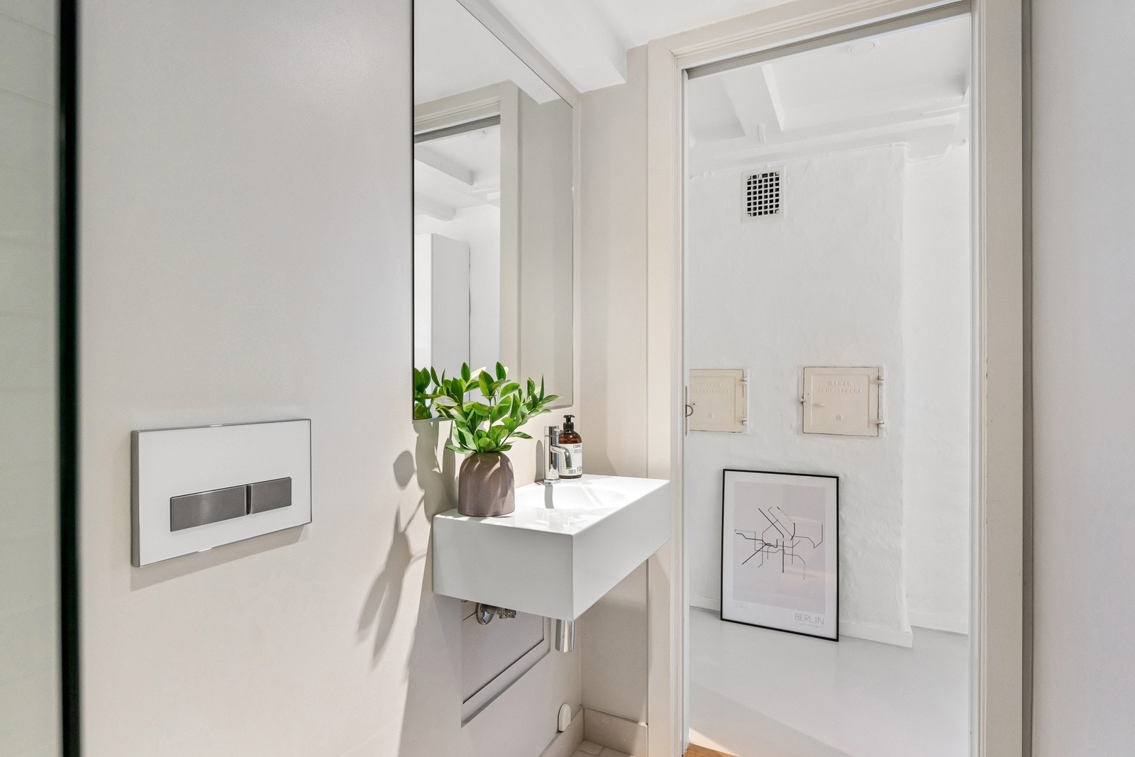 Videre er det en veggmontert servant, stort servantspeil og et veggmontert toalett. Badet har beige fliser på gulv med gulvvarme, downlights, lysmalte vegger og lekre veggfliser i dusjsonen. Galleribilde