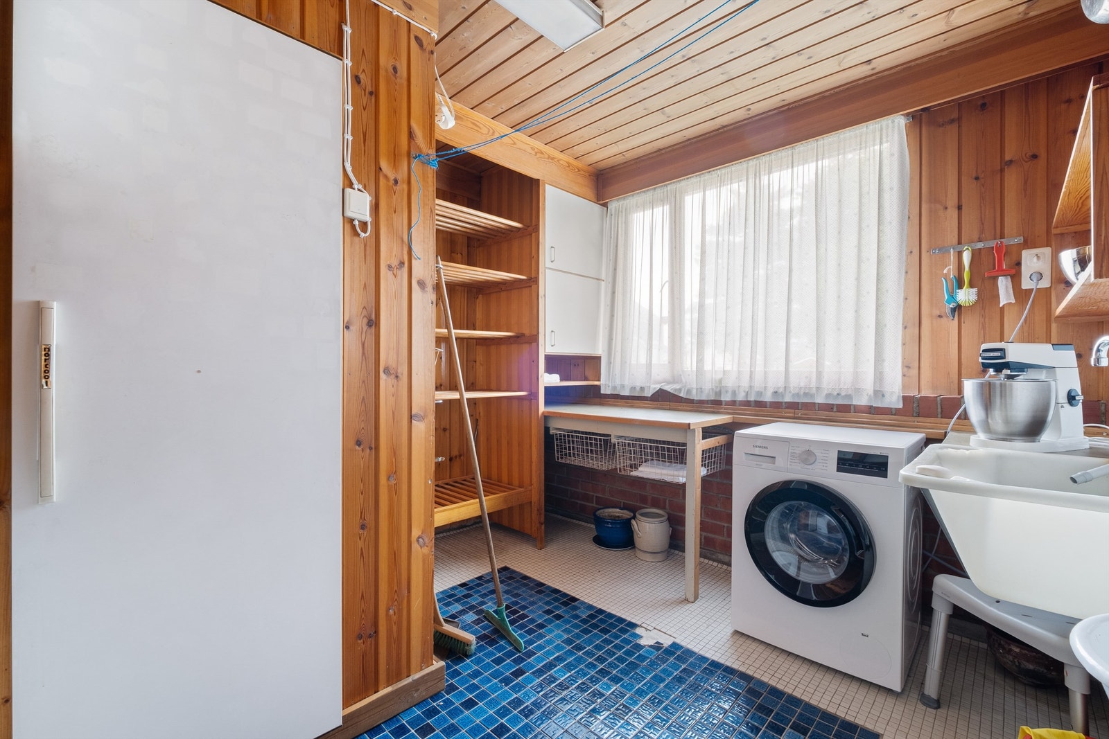 Bak kjøkkenet befinner det seg et vaskerom innredet med utslagsvask, skap og hyller, samt opplegg for vaskemaskin. Galleribilde