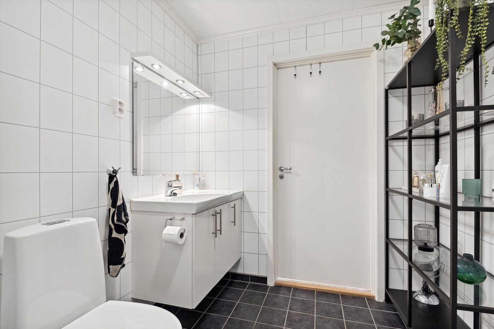 Tidløs baderomsinnredning med lyse fronter og heldekkende servant, speil med belysning over. Baderommet er også utstyrt med dusjhjørne med innfellbare glassdører og toalett. Plass og opplegg for vaskemaskin og tørketrommel over om ønskelig. Galleribilde