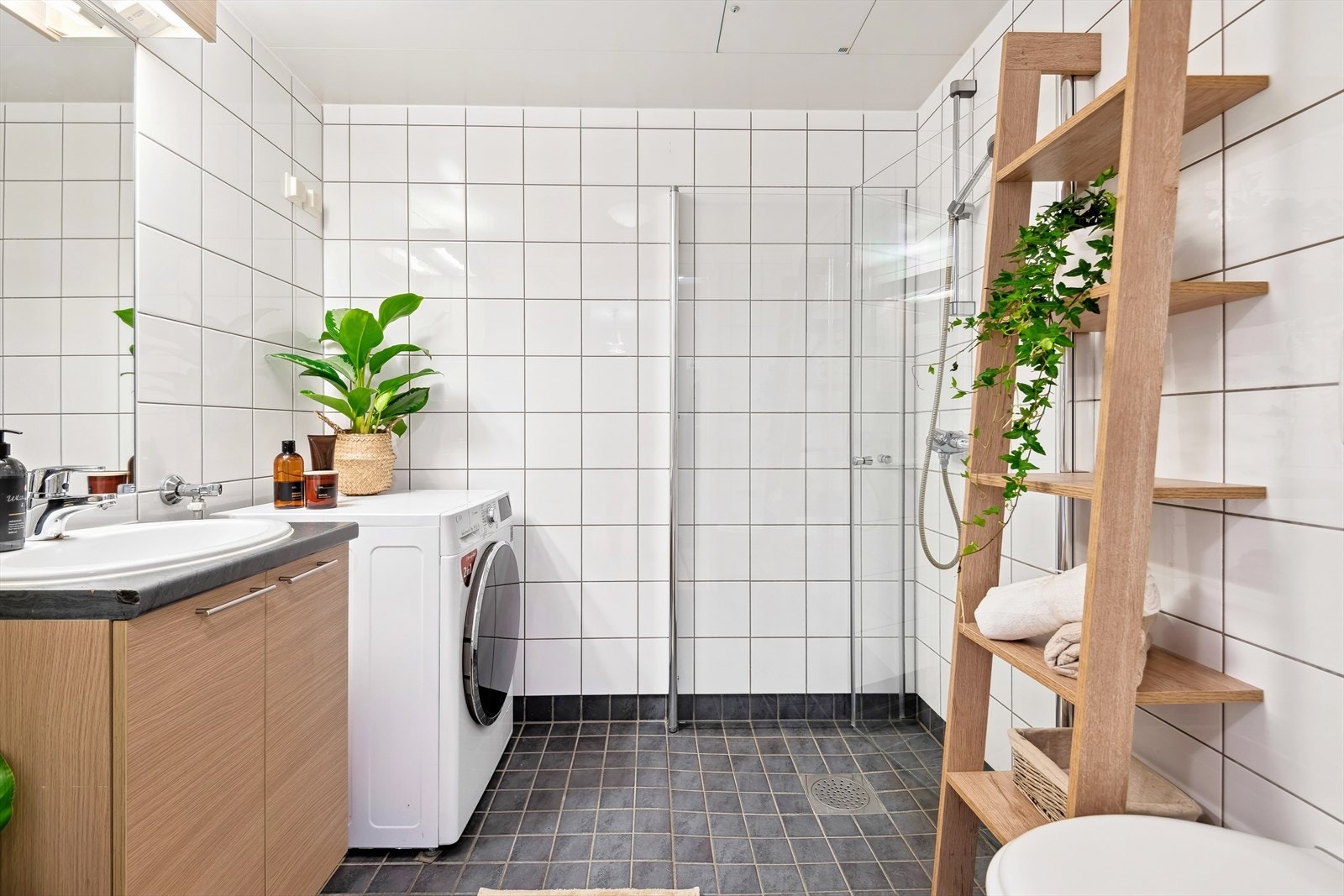 Lekkert bad med flislagte vegger og gulv med varmekabler. Badet har vegghengt wc, inn-/utadslående dusjdører og opplegg for vaskemaskin. Galleribilde