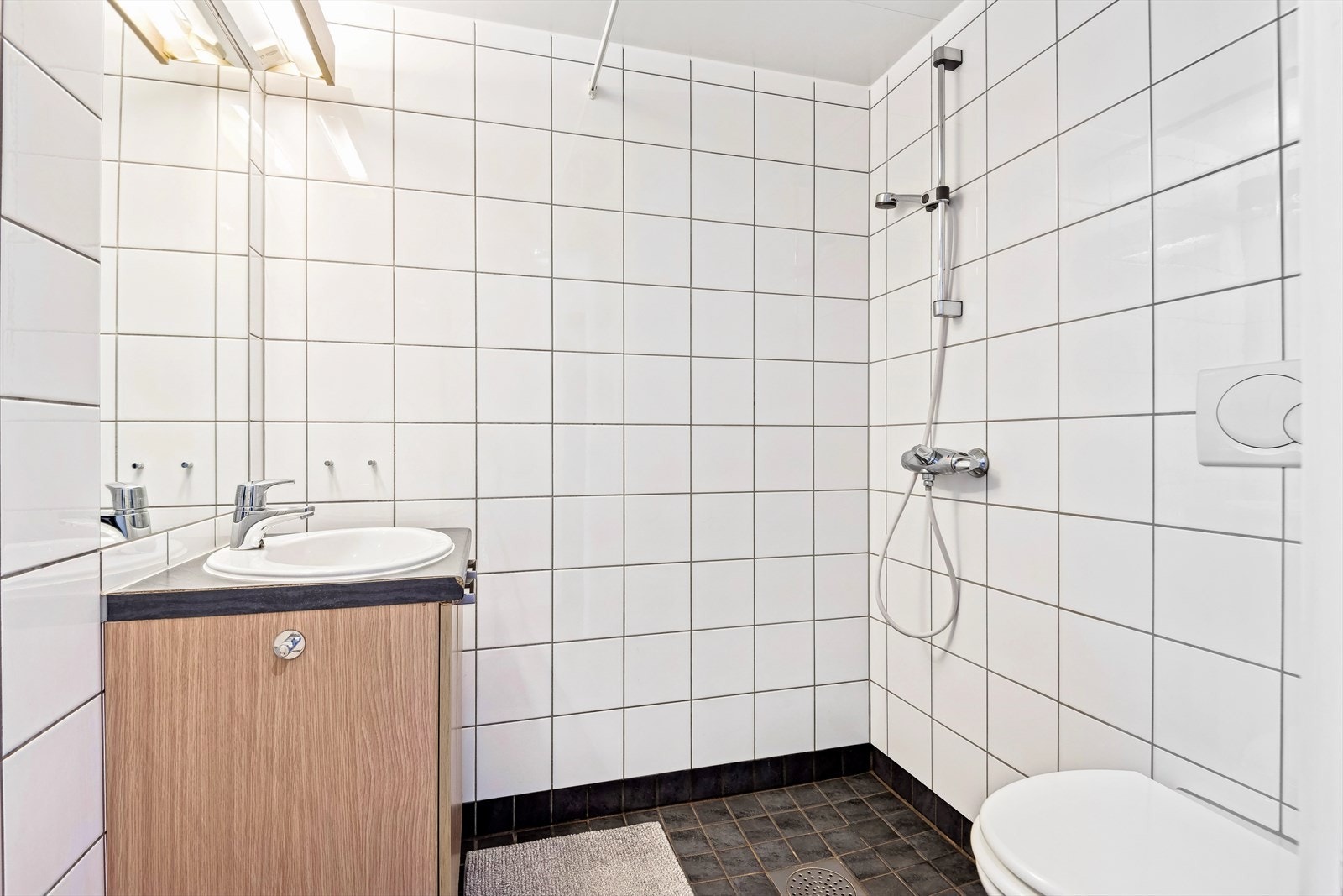 Utleiedel - Lyst bad med flislagte vegger og flislagt gulv med varmekabler. Badet består av vegghengt wc, servant m/underskap speil m/overlys og åpen dusj med opplegg for forheng. Galleribilde