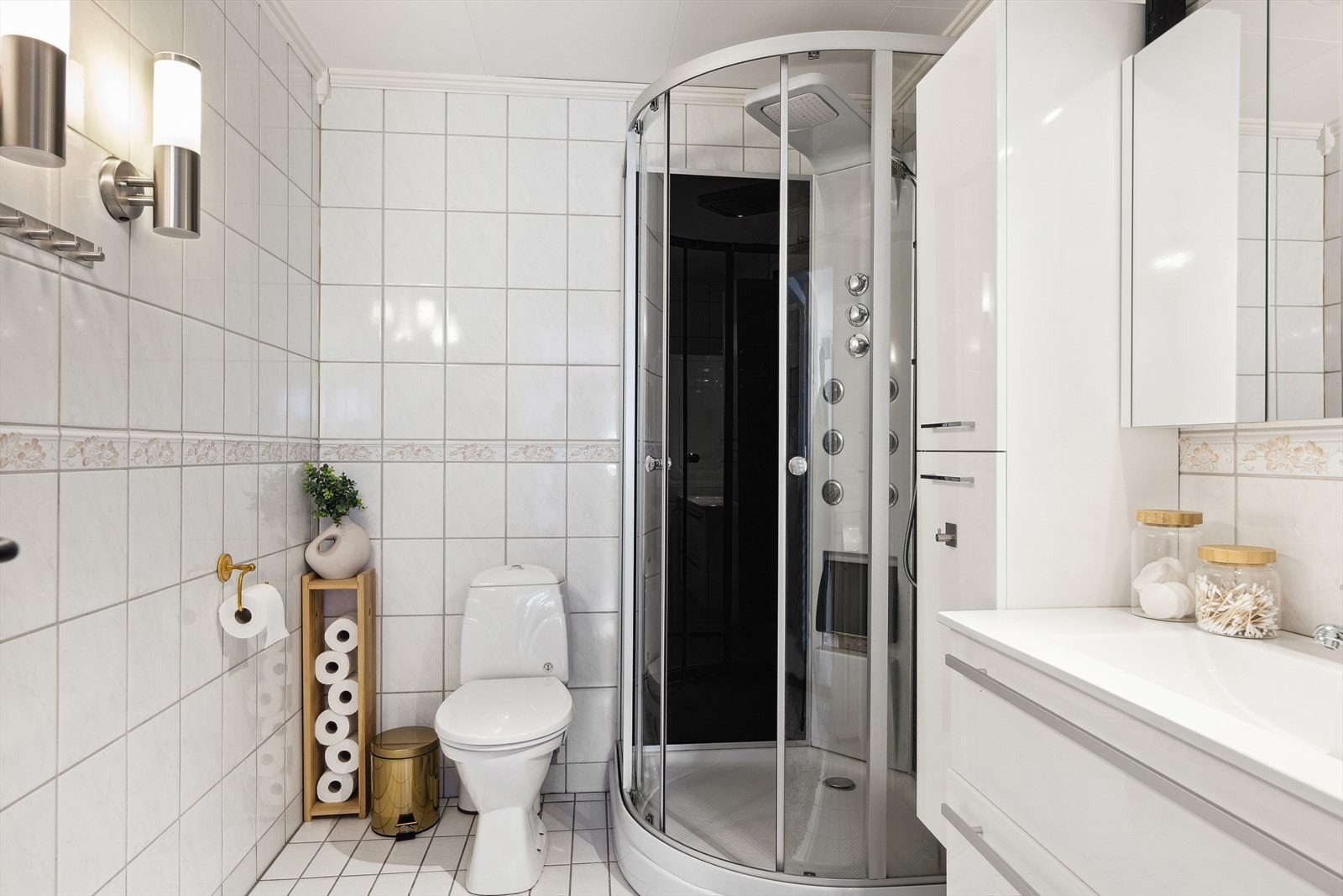 Badet er stilfullt innredet med fliser på vegg og gulv. Innredningen er moderne hvit med skuffer, speilskap og ekstra høyskap i tillegg Galleribilde