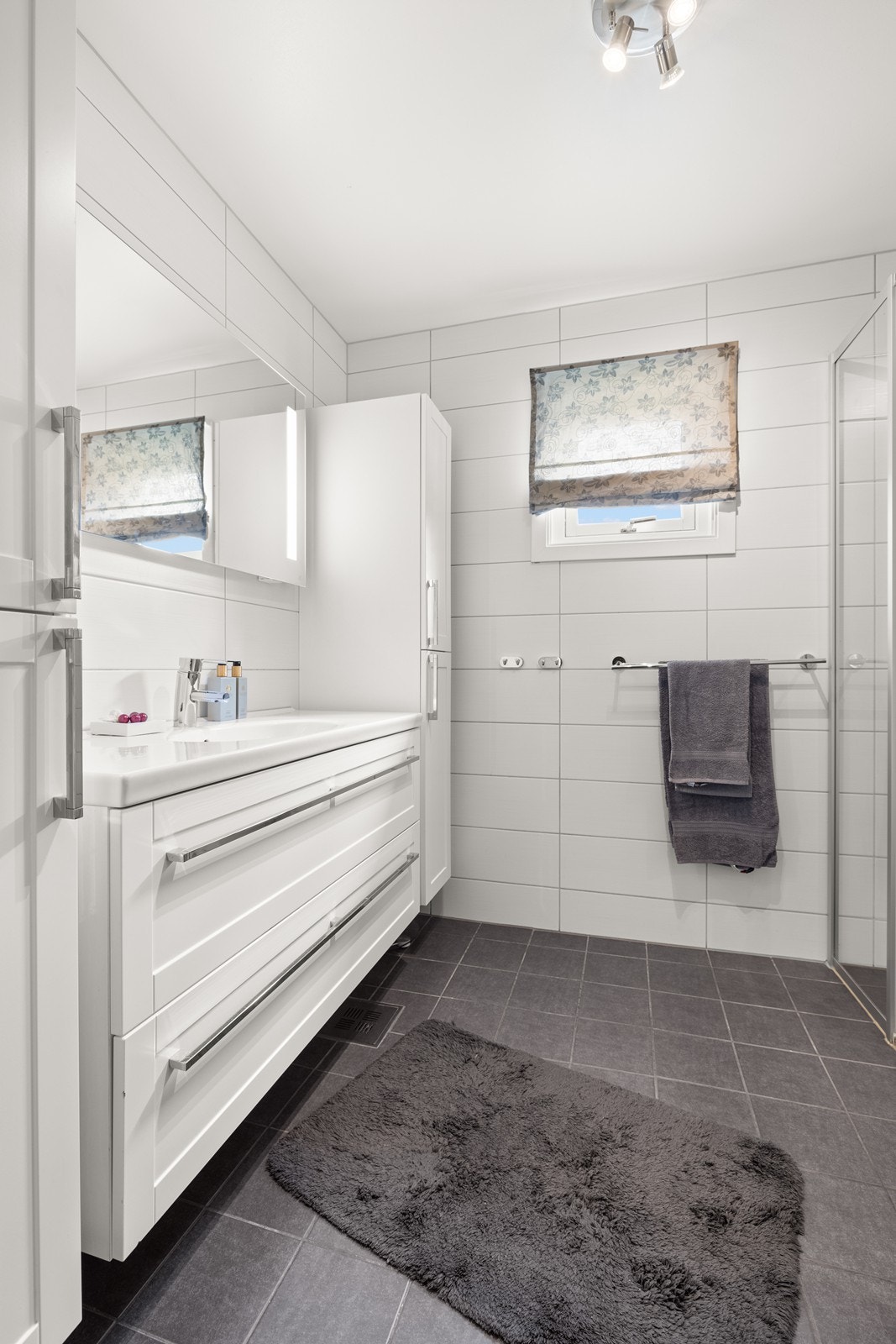 Pent flislagt bad med benkeskap og høyskap med profilerte fronter. Speil med belysning over servant. Galleribilde