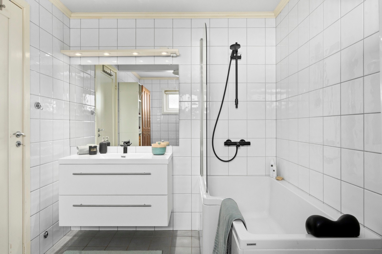 Baderomsinnredning med servant, speil med lys, wc og badekar med vegghengt badekararmatur Galleribilde