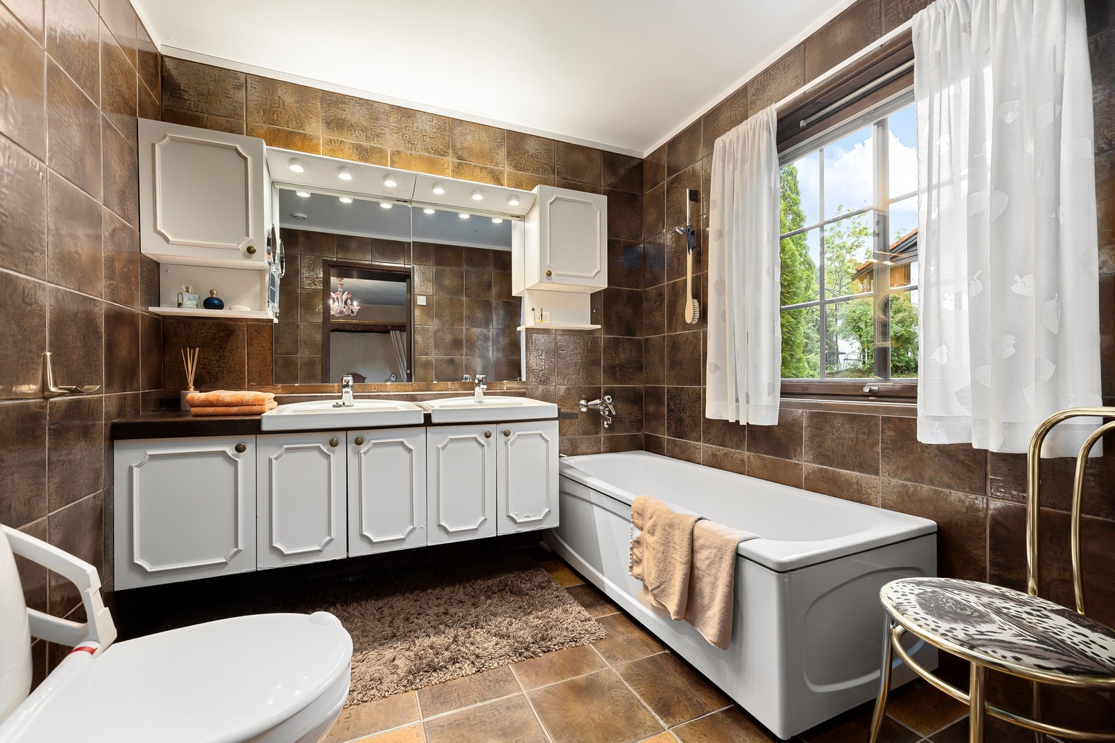 Eldre bad med badekar. Det er fliser på vegger og gulv med varmekabler Galleribilde