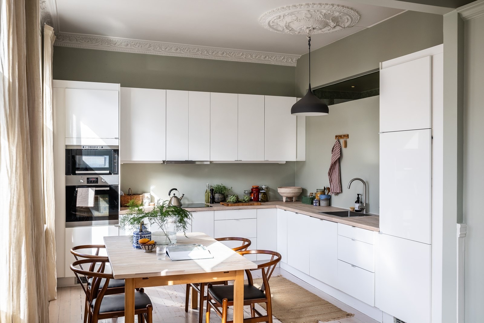 Ikea kjøkkeninnredning med hvite, glatte og lakkerte fronter og benkeplate i oljet treverk. Det er integrerte hvitevarer med induksjonstopp, stekeovn, mikrobølgeovn, oppvaskmaskin og kjøl/fryseskap. Galleribilde