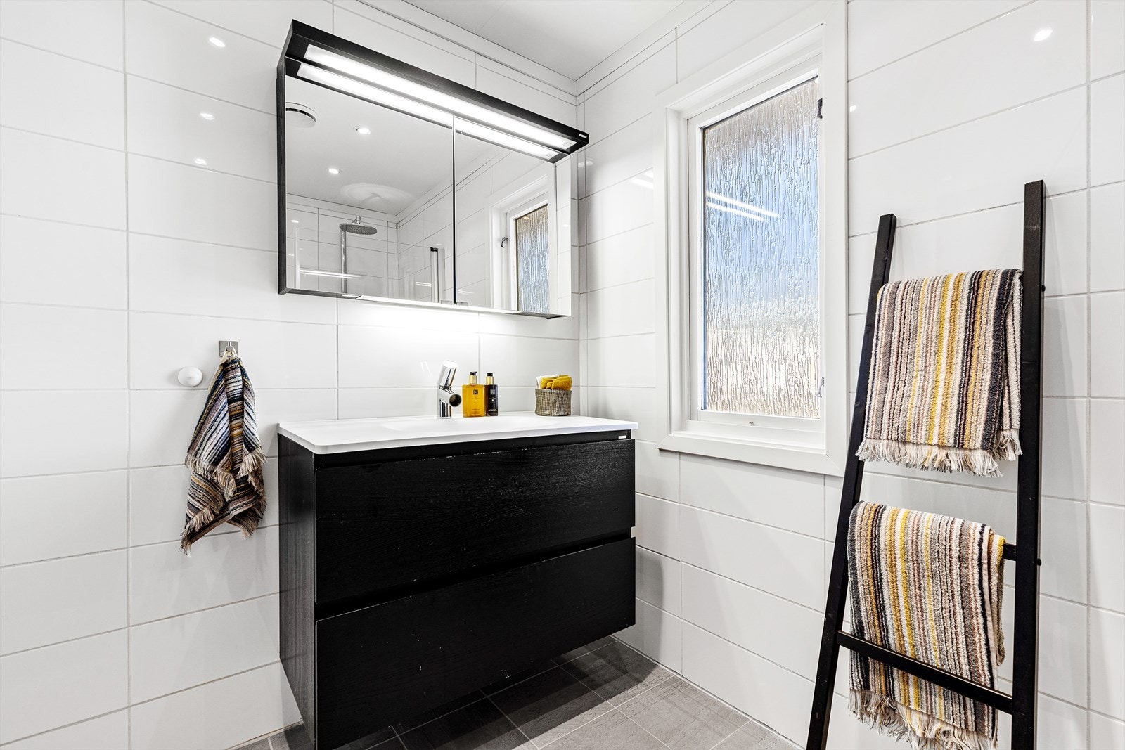 Badet i 1. etasje med vegghengt wc, servant med innredning og dusj med dusjdører i glass Galleribilde