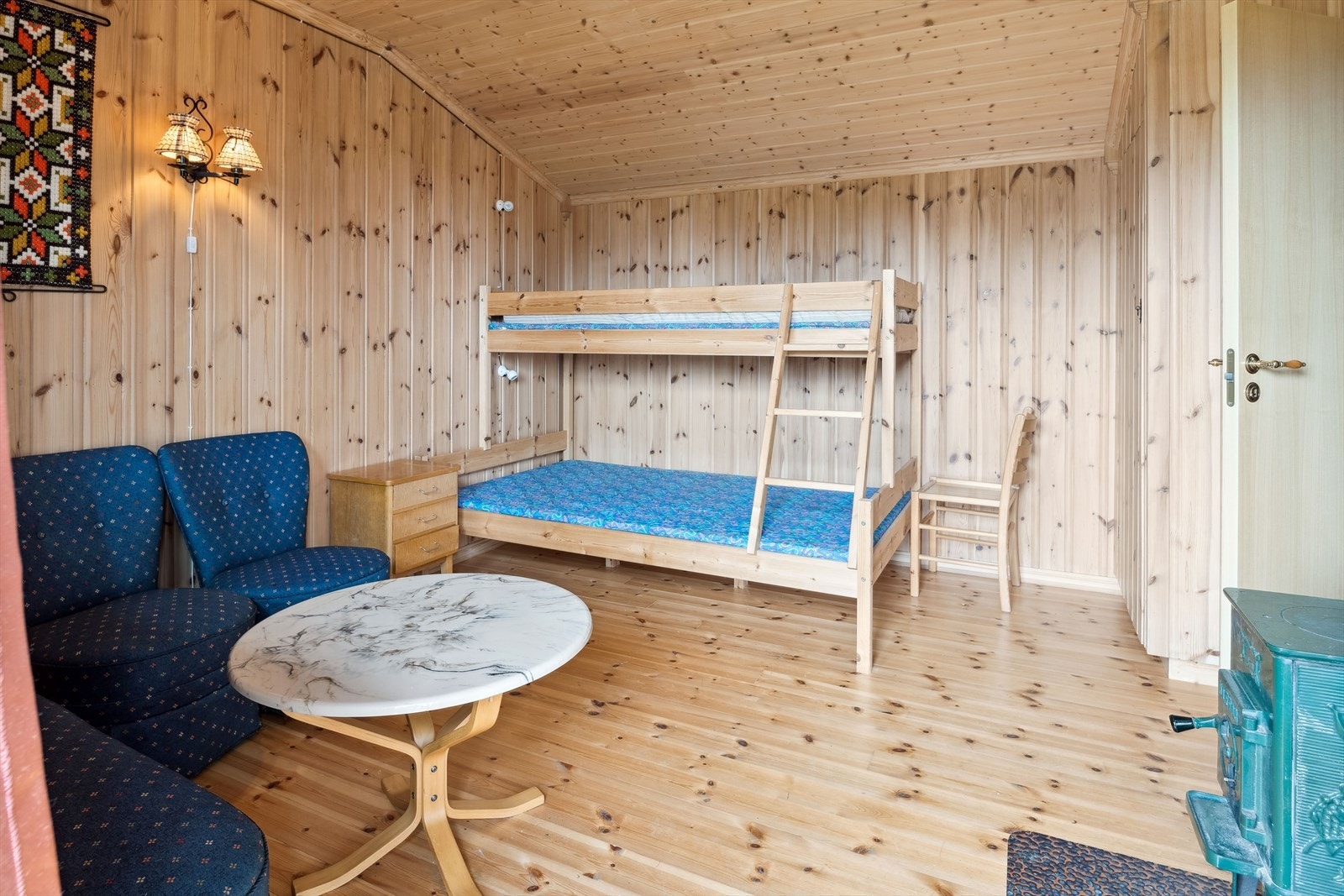 Gjesterom innredet med en køyeseng med 3 sengeplasser. Rommet har heltre furugulv, overflater med panel og en koselig vedovn. Galleribilde