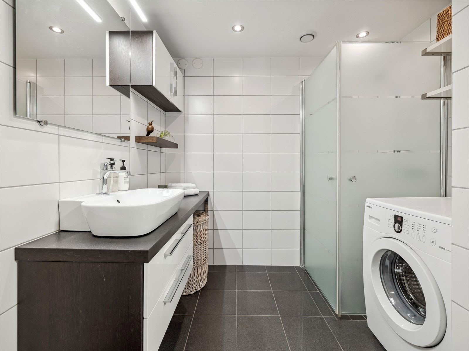 Baderomsinnredningen består av benkeskap/veggskap, speil og belysning over servant, dusj med innfellbare dører i herdet glass, servant og veggfestet klosett. Opplegg for vaskemaskin. Galleribilde