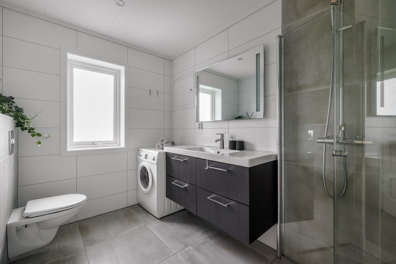 Lyst og pent, flislagt baderom med gulvvarme i 2. etasje. Badet har vegghengt toalett og åpen dusjløsning med innfellbare dusjvegger, samt opplegg for vaskemaskin. Galleribilde