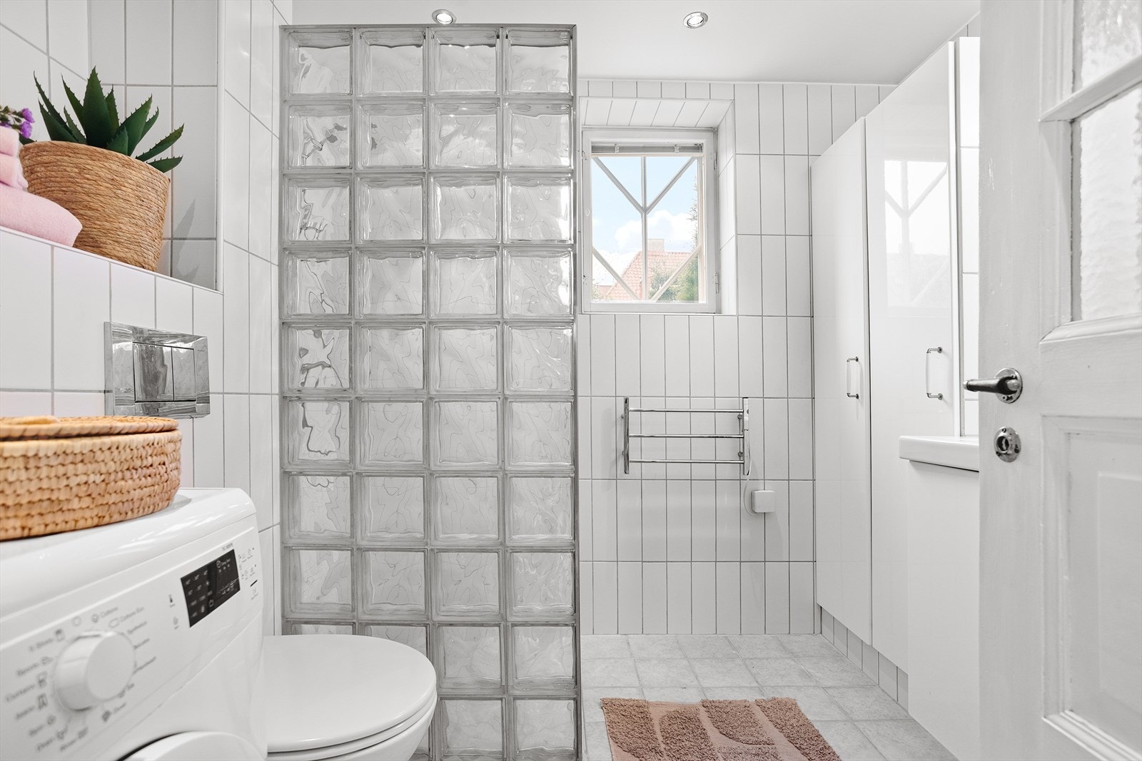 Badet er utstyrt med vegghengt wc, servantskap og dusj i hjørne med glassbyggerstensvegg. Galleribilde