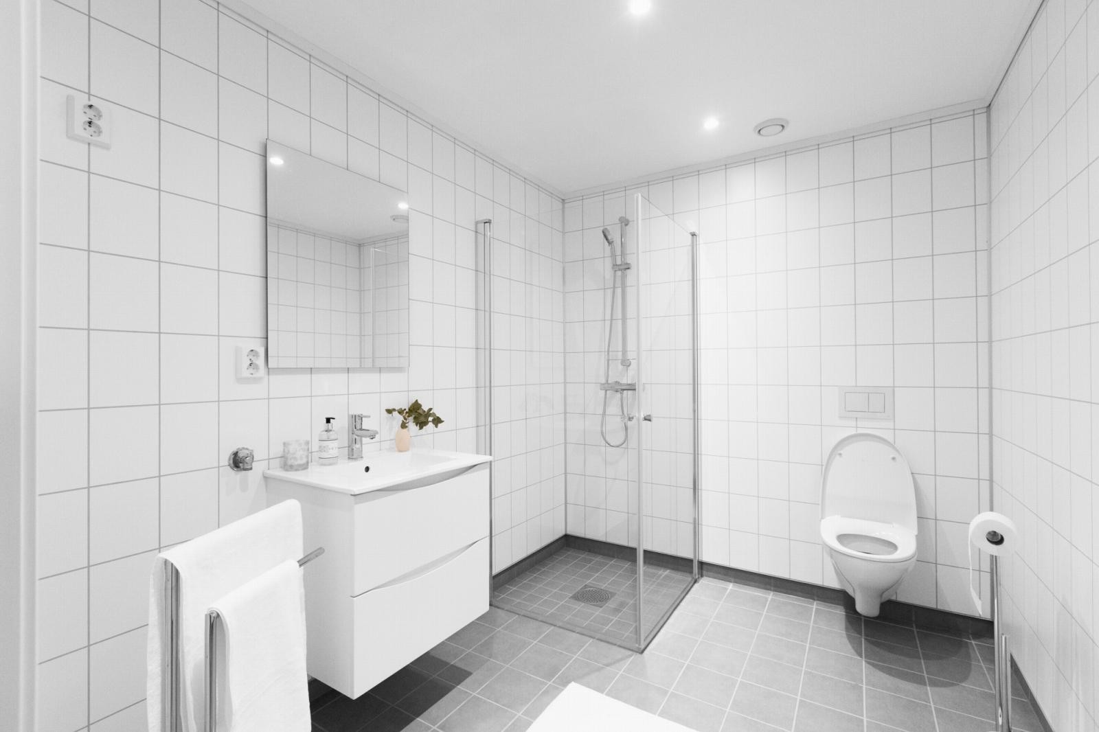Baderom med flislagt gulv og varmekabler. Avsatt plass til vaskemaskin. Utstyrt med servantinnredning, vegghengt toalett og dusj. Galleribilde